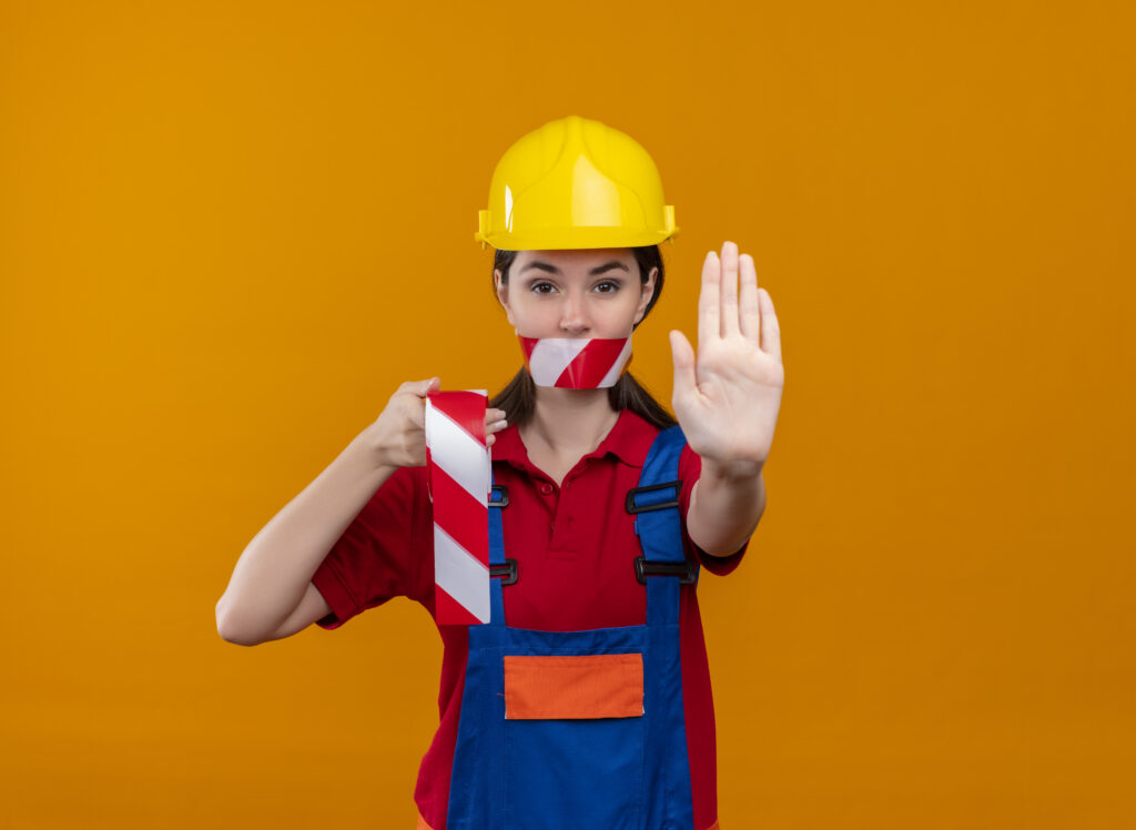Cvat blog | perigo x risco: a diferença que a nr-1 ensina e pouca gente aplica 1 Perigo x risco na segurança do trabalho: profissional com capacete fazendo gesto de parada e segurando fita de sinalização, representando prevenção de riscos conforme nr-1