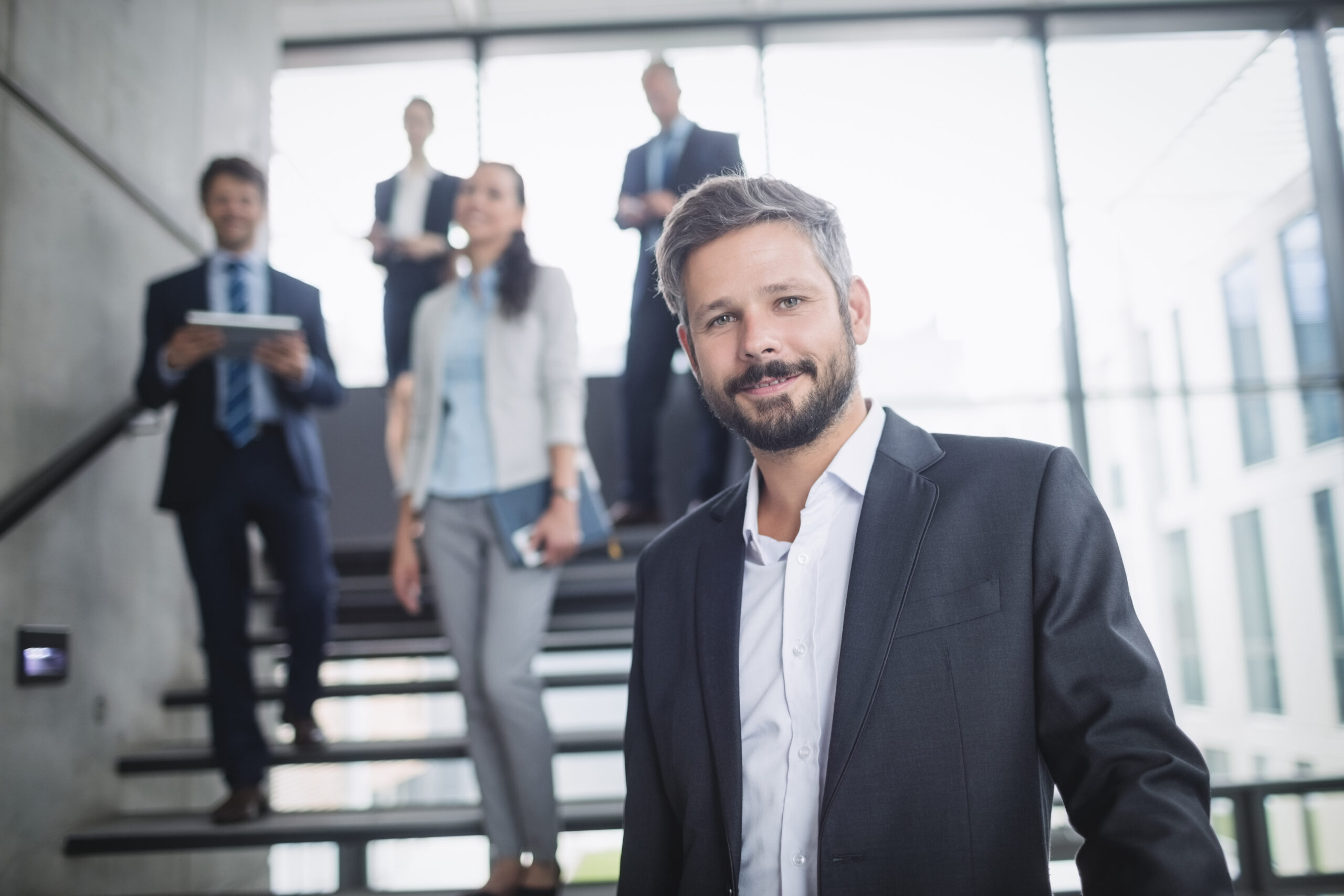 Homem confiante em destaque com fundo de colegas de trabalho borrados (profissões indistintas). Ela está avançando, liderando por ter um perfil comportamental mais compatível.