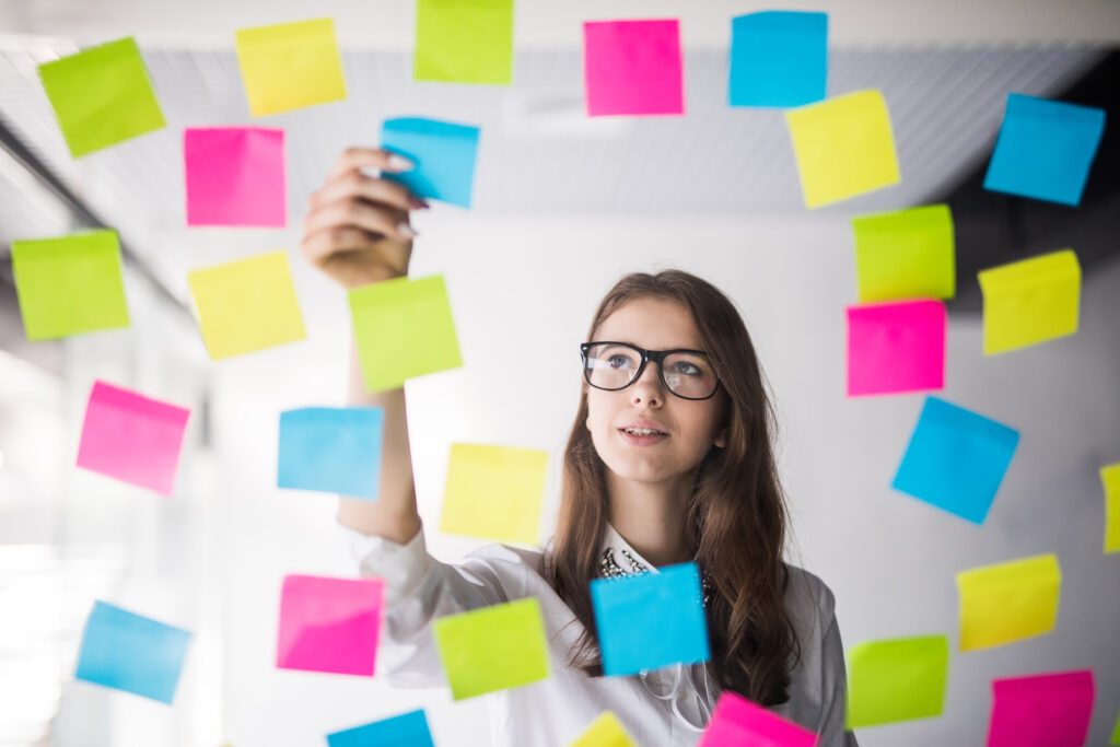 Imagem criativa de uma pessoa diante de um quadro de ideias com post-its coloridos, olhando estrategicamente com seu perfil comportamental